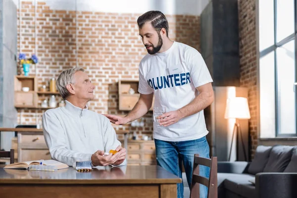 Zorg vrijwilliger het geven van een glas water aan een zieke gepensioneerde m/v — Stockfoto