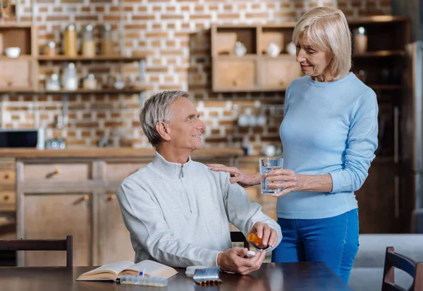 Liebende alte Frau gibt ihrem älteren Mann ein Glas Wasser — Stockfoto