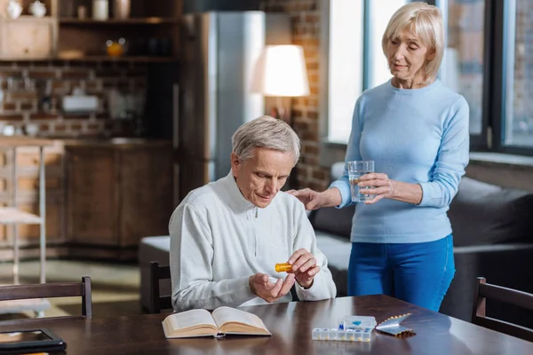 Hombre mayor concentrado contando sus pastillas antes de beber agua — Foto de Stock