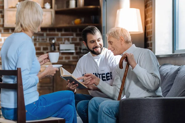 Feliz pensionista mostrando su libro favorito a un voluntario alegre — Foto de Stock