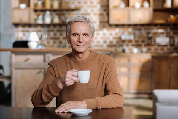 Lugn glad pensionär leende medan du sitter med ett tag cup — Stockfoto