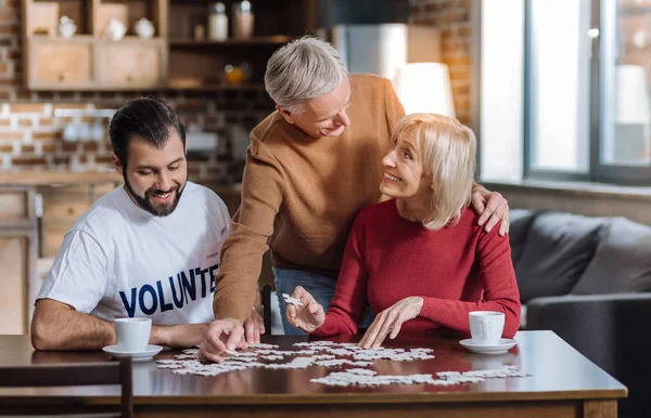 Positiv kvinna gör ett pussel med hennes kärleksfull make och deras volontär — Stockfoto