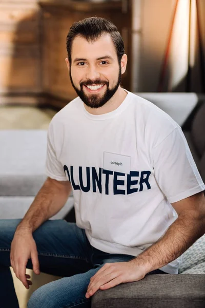 Feliz joven voluntario sentado en el sofá y sonriendo —  Fotos de Stock