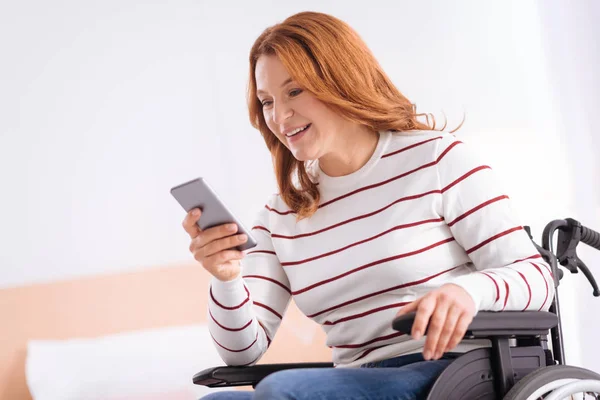 Mujer discapacitada sonriente en silla de ruedas con su teléfono — Foto de Stock