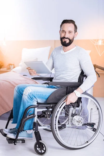 Homem alegre sentado Eu uma cadeira de rodas com um tablet — Fotografia de Stock