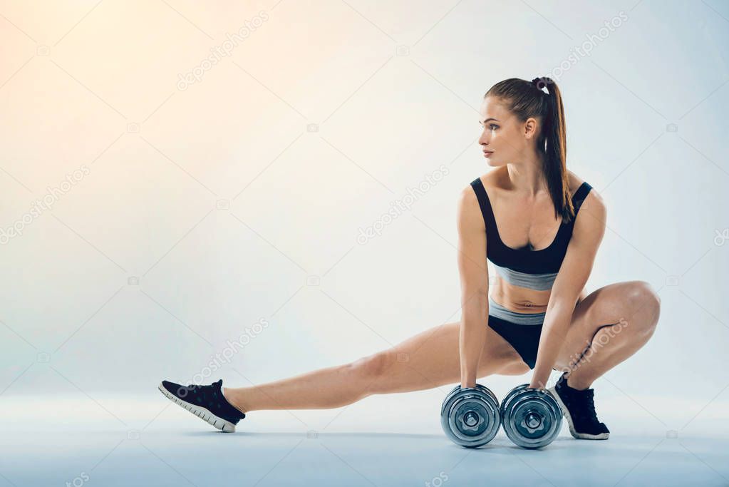 Attractive female athlete stretching with dumbbells