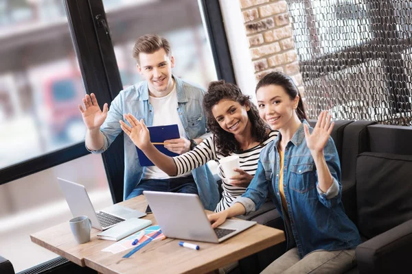 Felices amigos saludando mientras están sentados a la mesa — Foto de Stock