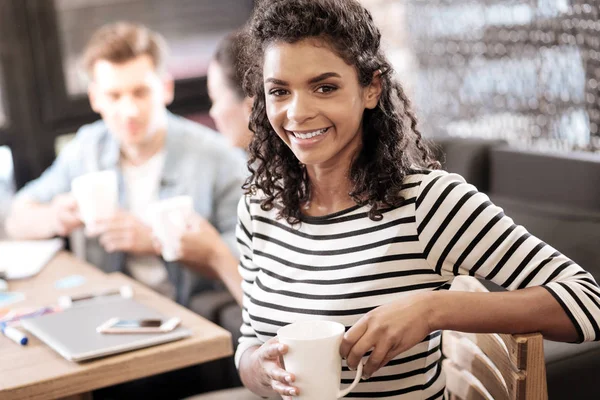 Blij krullend-haired donker-eyed meisje zit aan de tafel — Stockfoto