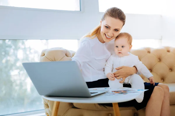 Relaxed woman pointing at the laptop while entertaining a baby — Stock Photo, Image