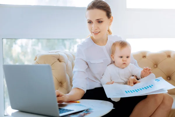 Entzückendes Baby beim Betrachten der Grafiken seiner geschäftigen arbeitenden Mutter — Stockfoto