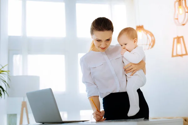 Arbetande kvinna att göra anteckningar med ett barn i famnen — Stockfoto