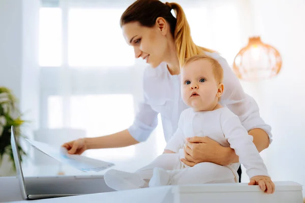 Attentive calm woman working while sitting with a baby — Stock Photo, Image