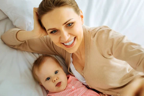 Positiv mor gør sjove ansigter med sin lille baby - Stock-foto