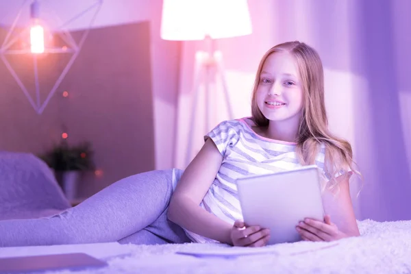 Веселая девушка лежит на кровати со своим планшетом — стоковое фото