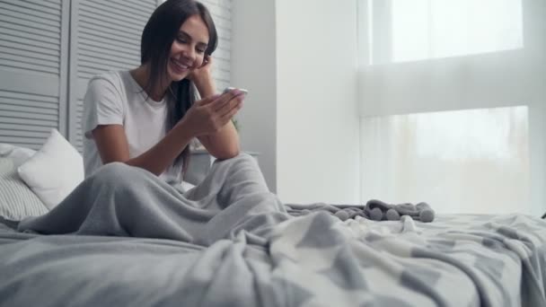 Радостная молодая женщина болтает в постели — стоковое видео