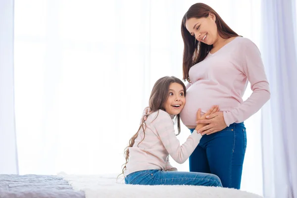 Sorprendida niña pequeña sorprendida al escuchar al bebé en la barriga de las mamás —  Fotos de Stock