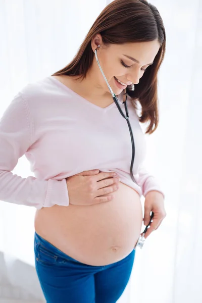 Entzückende schwangere Frau versucht, ihr Baby zu hören — Stockfoto