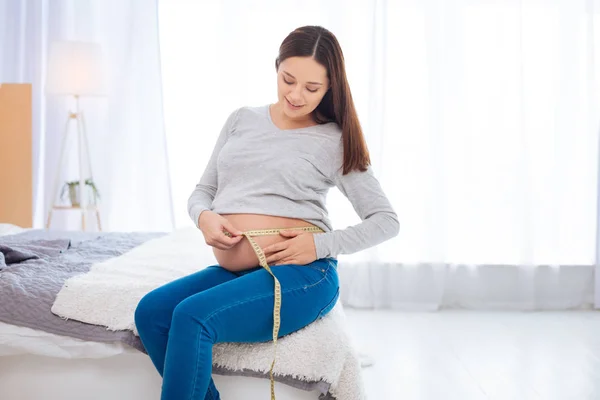 Положительная беременная женщина, считающая сантиметры — стоковое фото