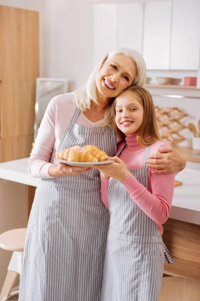 Весела літня жінка, що стоїть з онукою на кухні — стокове фото
