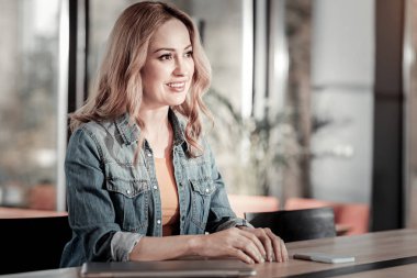 Gülümseyen bir kafede oturan ve bir garson için bekleyen genç kadın