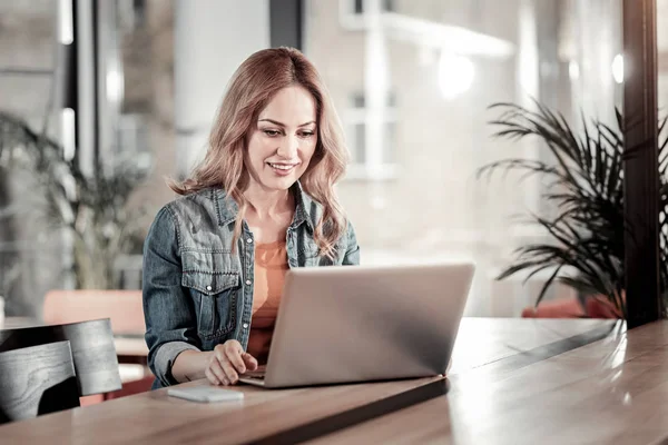 Smarta unga kvinnan ler och tittar på hennes laptop — Stockfoto