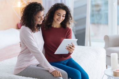 Tablet bilgisayarda bakarken gülümseyen rahat kıvırcık saçlı kız kardeş