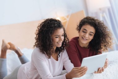 Touchpad ile yatakta yatarken ve gülümseyen güzel kadın kardeşler