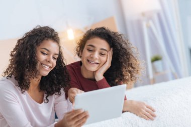Genel olarak tablet bilgisayar kullanırken sırıtarak kıvırcık saçlı kız