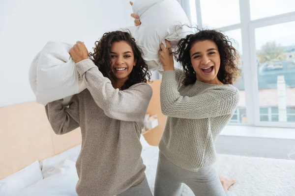 Hermanas alegres sonriendo mientras se preparan para la pelea de almohadas —  Fotos de Stock