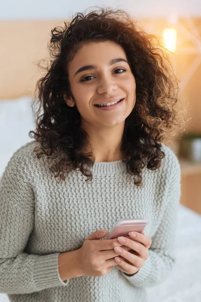 Chica de pelo rizado bonito con teléfono inteligente sonriendo alegremente — Foto de Stock