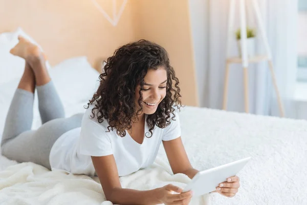 Joyeuse fille rayonnant tout en étant couché sur le lit et en utilisant le pavé tactile — Photo