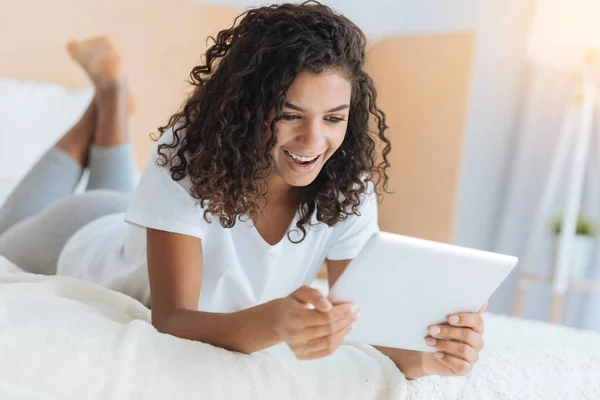 Чрезвычайно счастливая девушка улыбается, глядя на планшетный компьютер — стоковое фото