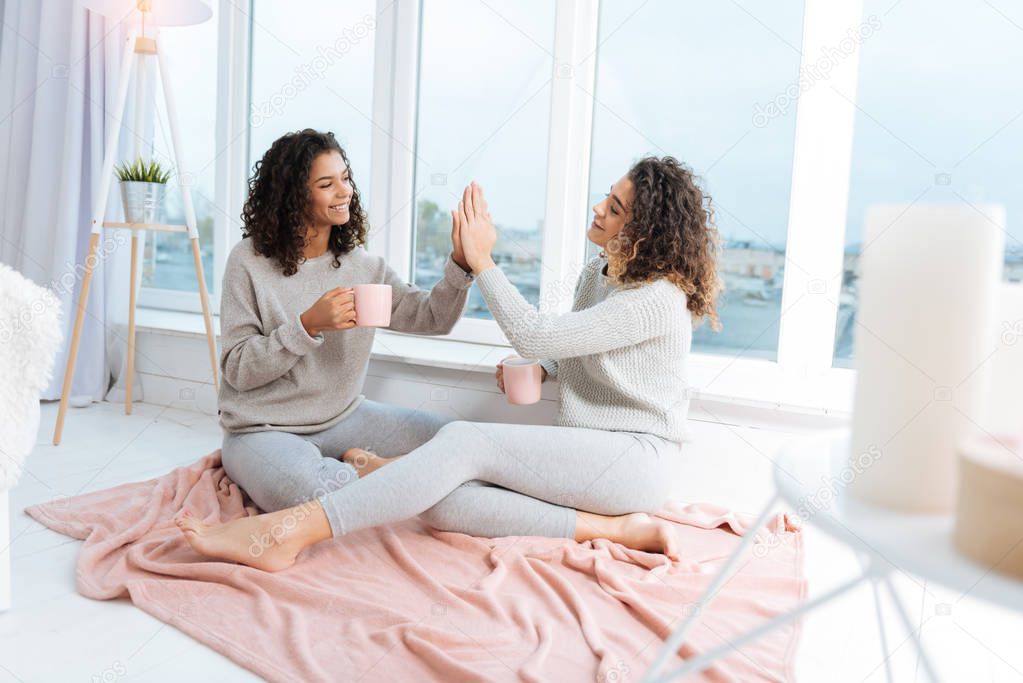 Relaxed sisters high fiving while drinking tea