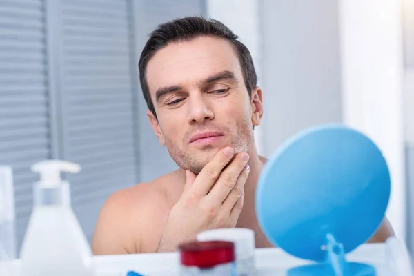 Schöner konzentrierter Mann, der sein Gesicht untersucht — Stockfoto