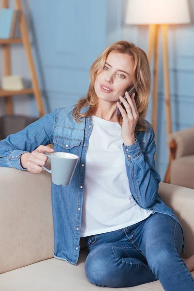 Lugn ung kvinna sitter på en soffa och pratar på en telefon — Stockfoto