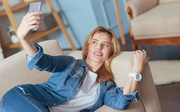 Внимательная красивая женщина держит смартфон во время позирования — стоковое фото