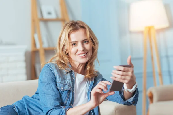 Söt ung kvinna leende medan du sitter med en smart telefon — Stockfoto
