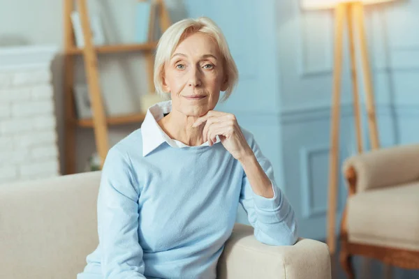 Positive Seniorin sitzt auf Sofa und lächelt fröhlich — Stockfoto