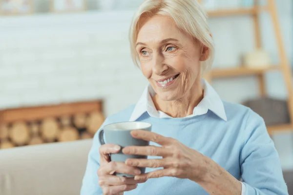 Alegre mujer mayor sonriendo mientras sostiene su taza favorita — Foto de Stock