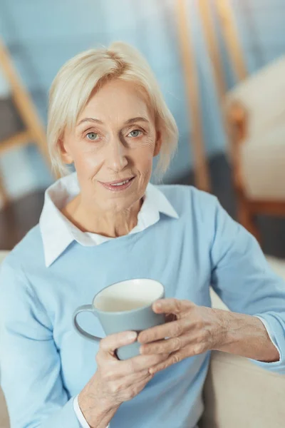 Ältere Frau fühlt sich mit ihrem leckeren Tee zufrieden, während sie zu Hause sitzt — Stockfoto