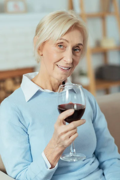 Щаслива літня жінка п'є червоне вино і посміхається люб'язно — стокове фото