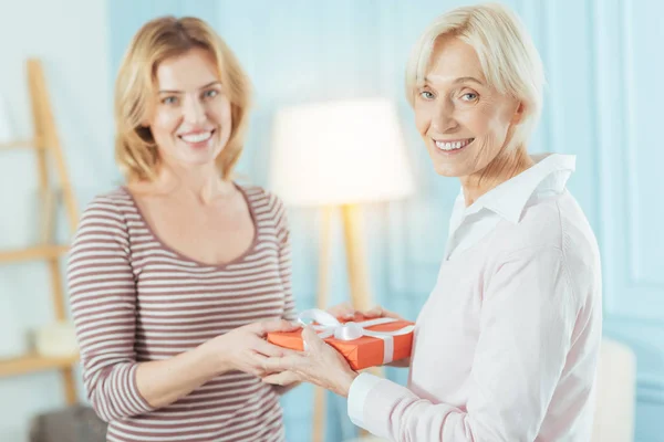 Cute cheerful women standing and holding a beautiful present together — Stock Photo, Image