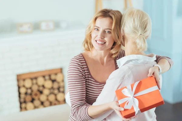 Beautiful young woman holding a present while greeting her relative — Stock Photo, Image