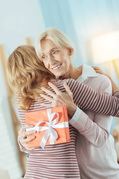 Happy wieku kobieta gospodarstwa jasny prezent przy przytulaniu jej względna — Zdjęcie stockowe