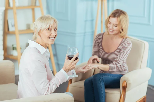 Позитивная пожилая женщина пьет вино и любуется красивым кольцом — стоковое фото