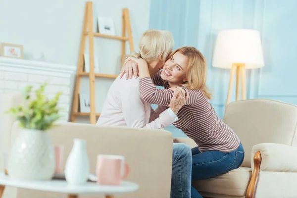 Kärleksfull mormor sitter på en soffa samtidigt en sondotter kramar henne — Stockfoto