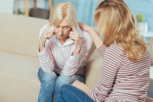 Aged woman sitting and touching her head while feeling unwell — Stock Photo, Image