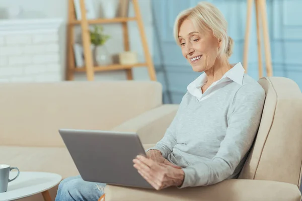 Прогрессивная пожилая женщина наслаждается своим новым ноутбуком и улыбается — стоковое фото