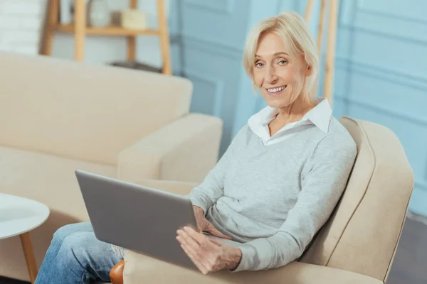 Щаслива старша жінка виглядає щасливою, тримаючи великий ноутбук — стокове фото