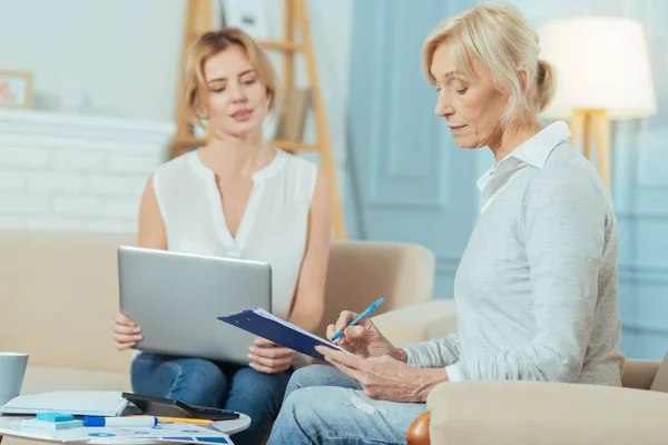 Attentive aged woman being concentrated while putting her signature